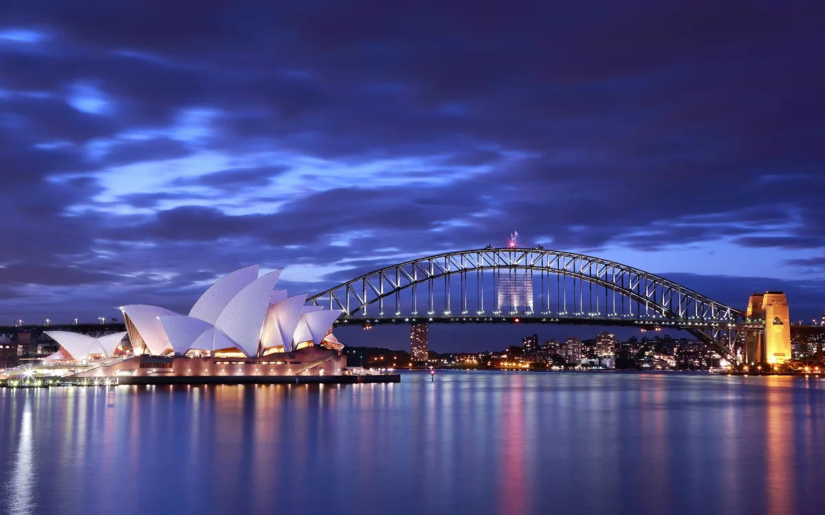 Sydney Opera House and Harbour Bridge lit up at dusk, reflected in the harbour